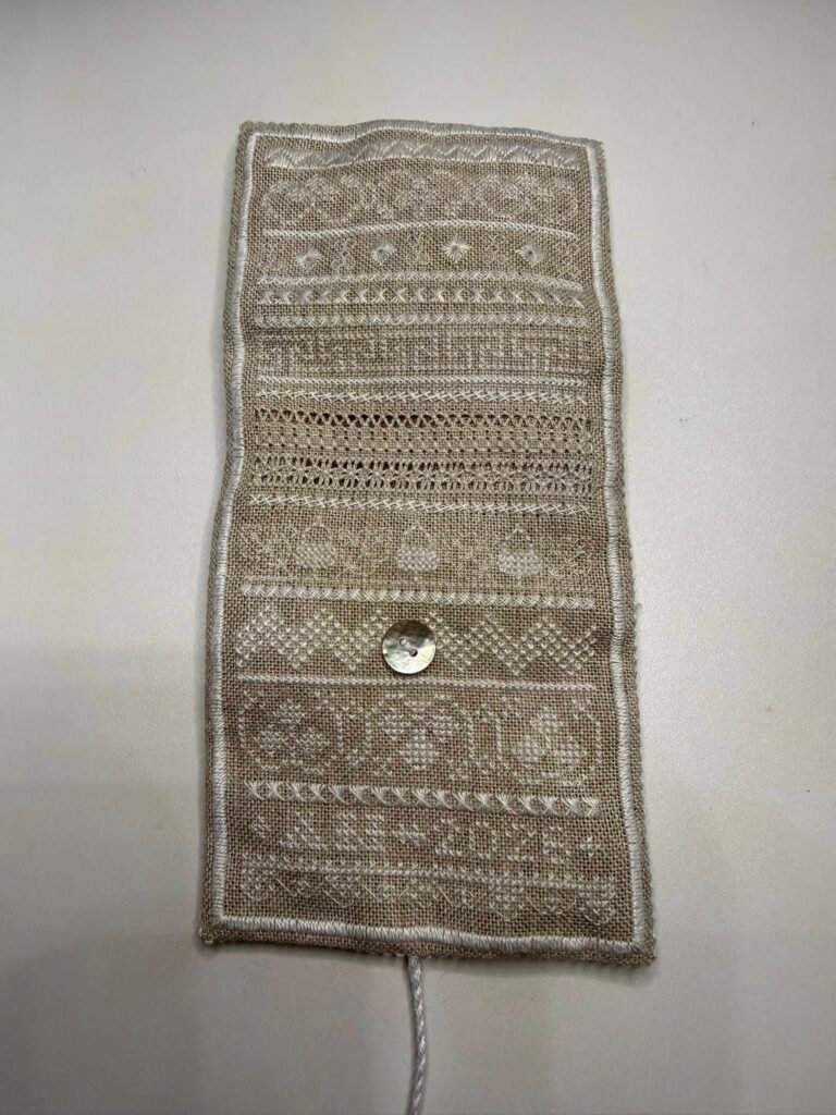A fawn colored rectangle of linen embroidered in a range of stitches in cream threads