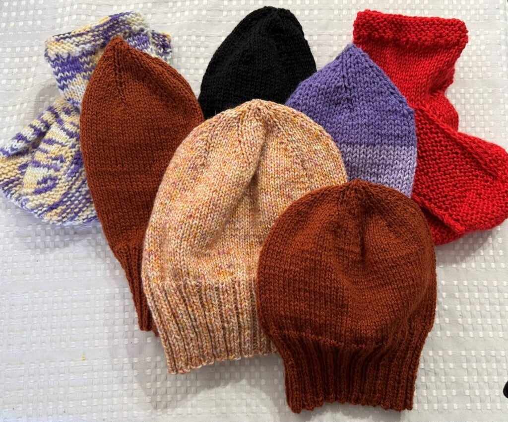 four knitted beanies in browns and purple with two pairs of knitted slippers in red and variegated purple