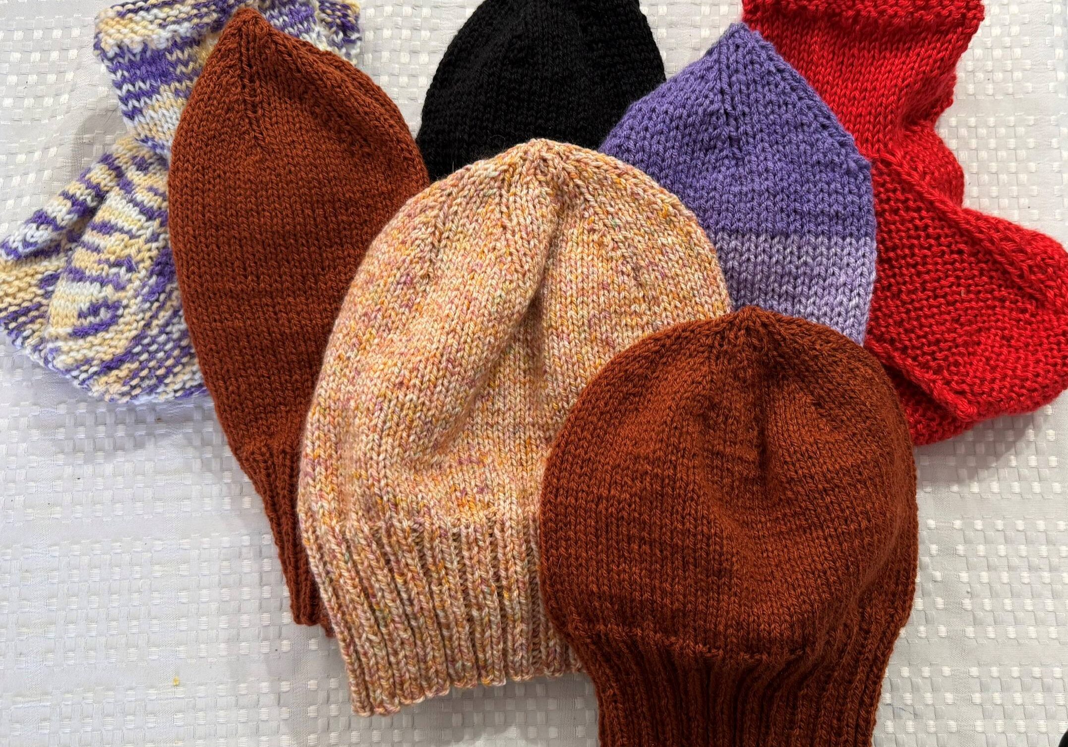 four knitted beanies in browns and purple with two pairs of knitted slippers in red and variegated purple