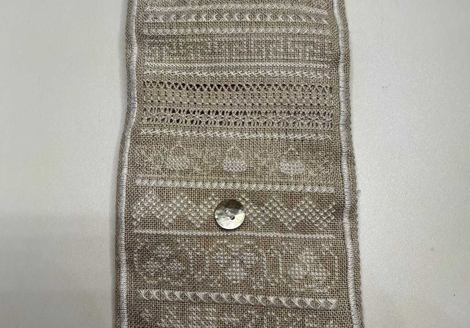A fawn colored rectangle of linen embroidered in a range of stitches in cream threads